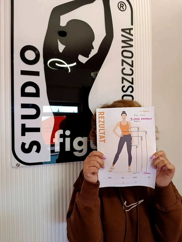 Osoba z kartą rezultatu na tle oznakowania Studio Figura Włoszczowa
